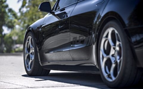 Front angle shot of a 2024 Tesla Model 3 Performance in black, equipped with 19-inch Satin Titanium UP-05 Forged Wheels by Unplugged Performance, captured in a sunny parking lot.