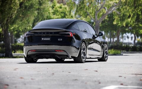 Rear angle view of a 2024 Tesla Model 3 Performance in black, showcasing 19-inch Satin Titanium UP-05 Forged Wheels by Unplugged Performance, set against a backdrop of palm trees.