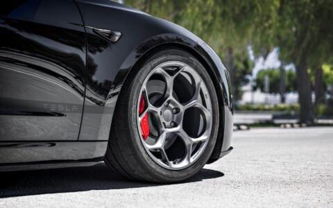 Front angle view of a 2024 Tesla Model 3 Performance in black, featuring 19-inch Satin Titanium UP-05 Forged Wheels by Unplugged Performance, parked under palm trees in a modern setting.