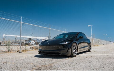 Tesla Model 3 Performance with 19-inch Satin Titanium UP-05 Forged Wheels by Unplugged Performance, parked in front of an industrial backdrop, highlighting the car’s sleek design and high-performance wheels.