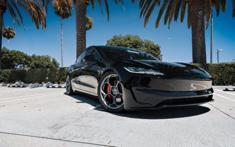 Front angle view of a 2024 Tesla Model 3 Performance in black, featuring 19-inch Satin Titanium UP-05 Forged Wheels by Unplugged Performance, parked under palm trees in a modern setting.