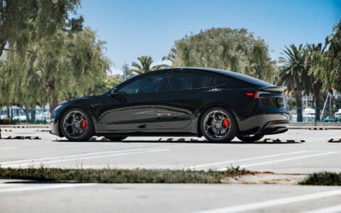 Rear angle view of a 2024 Tesla Model 3 Performance in black, showcasing 19-inch Satin Titanium UP-05 Forged Wheels by Unplugged Performance, set against a backdrop of palm trees.
