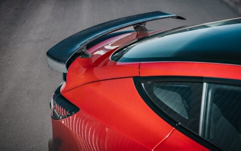 2024 Tesla Model 3 Performance in Ultra Red featuring a sleek carbon fiber wing spoiler by Unplugged Performance, parked in an industrial setting.