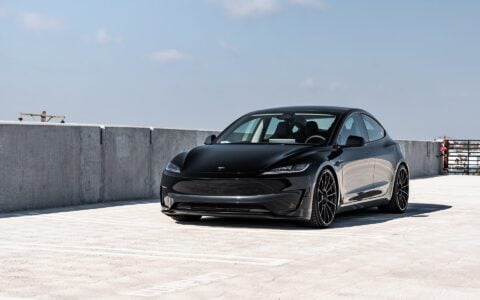 Front side view of a black Tesla Model 3 Performance featuring 21-inch Gloss Black UP-03 wheels by Unplugged Performance, parked in a rooftop parking lot under an overcast sky.