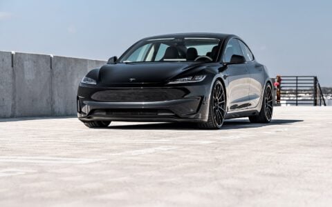 Front side view of a black Tesla Model 3 Performance featuring 21-inch Gloss Black UP-03 wheels by Unplugged Performance, parked in a rooftop parking lot under an overcast sky.