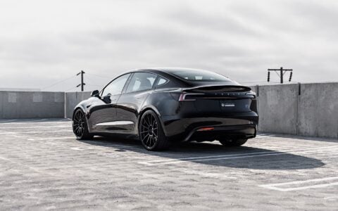 Rear side view of a black Tesla Model 3 Performance featuring 21-inch Gloss Black UP-03 wheels and red brake calipers by Unplugged Performance, parked in a rooftop parking lot under an overcast sky.