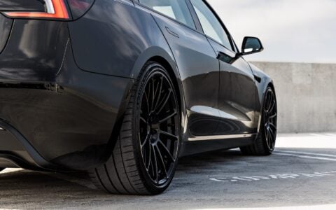 Rear side view of a black Tesla Model 3 Performance featuring 21-inch Gloss Black UP-03 wheels by Unplugged Performance, parked on a rooftop parking lot under a partly cloudy sky.