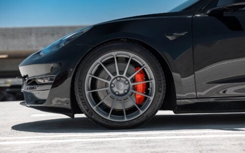 Close-up of the Tesla Model 3 Performance featuring red Tesla brake calipers paired with UP-03 wheels in Satin Titanium for superior braking and style.