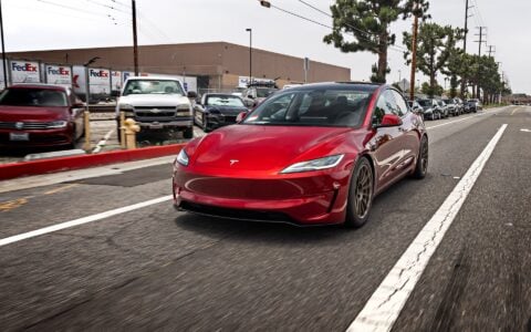 2024 Ultra Red Tesla Model 3 Performance driving on the road, equipped with 18-inch Satin Bronze UP-03 Forged Wheels by Unplugged Performance.