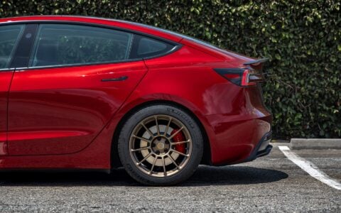 Close-up of the rear wheel of a 2024 Ultra Red Tesla Model 3 Performance, featuring 18-inch Satin Bronze UP-03 Forged Wheels by Unplugged Performance.