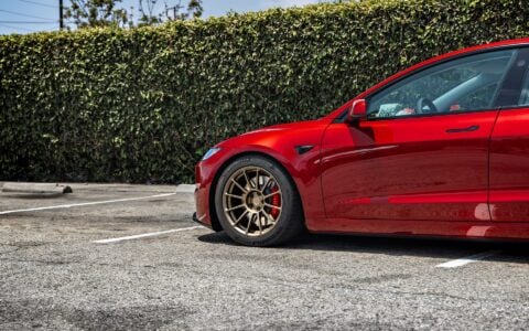 Close-up side view of a parked 2024 Tesla Model 3 Performance in Ultra Red, highlighting the front 18-inch Satin Bronze UP-03 Forged Wheel by Unplugged Performance.