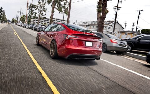 Rear view of a 2024 Tesla Model 3 Performance in Ultra Red on city street, featuring 18-inch Satin Bronze UP-03 Forged Wheels from Unplugged Performance.