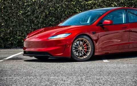 Close-up of the front wheel of a 2024 Tesla Model 3 Performance in Ultra Red, showcasing the 18-inch Satin Bronze UP-03 Forged Wheels by Unplugged Performance.