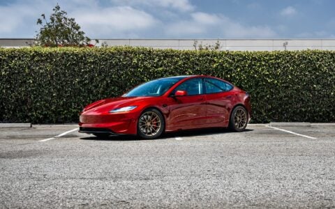 3/4 shot of a parked 2024 Tesla Model 3 Performance in Ultra Red, featuring 18-inch Satin Bronze UP-03 Forged Wheels by Unplugged Performance.