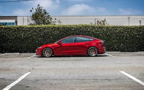 Side view of a 2024 Ultra Red Tesla Model 3 Performance parked, featuring 18-inch Satin Bronze UP-03 Forged Wheels by Unplugged Performance.