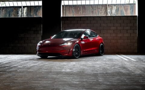 Profile view of an Ultra Red Tesla Model 3 Performance equipped with 19-inch Gloss Black UP-03 forged wheels by Unplugged Performance, parked against a wall.