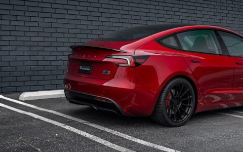 Angled rear view of an Ultra Red Tesla Model 3 Performance with 19-inch Gloss Black UP-03 forged wheels by Unplugged Performance, parked next to a black brick wall.