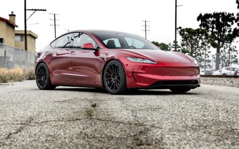 Angled front view of an Ultra Red Tesla Model 3 Performance showcasing 19-inch Gloss Black UP-03 forged wheels by Unplugged Performance, parked on an urban street.