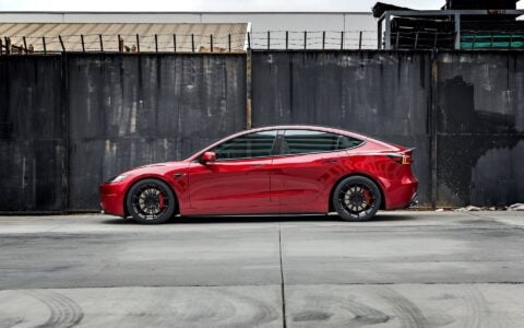 Side profile view of an Ultra Red Tesla Model 3 Performance showcasing 19-inch Gloss Black UP-03 forged wheels by Unplugged Performance, parked on an urban street.