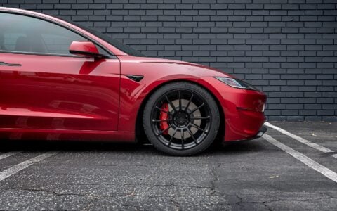 Close-up of the front wheel of an Ultra Red Tesla Model 3 Performance with 19-inch Gloss Black UP-03 forged wheels by Unplugged Performance, highlighting the wheel design and red brake calipers.