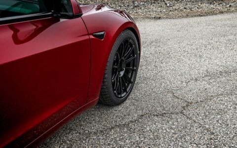 Side view of an Ultra Red Tesla Model 3 Performance showcasing 19-inch Gloss Black UP-03 forged wheels by Unplugged Performance, parked on a gravel surface.