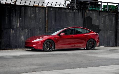 Profile view of an Ultra Red Tesla Model 3 Performance equipped with 19-inch Gloss Black UP-03 forged wheels by Unplugged Performance, parked against a black brick wall.