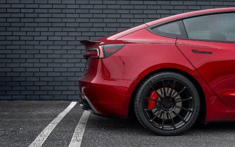 Close-up of the rear wheel of an Ultra Red Tesla Model 3 Performance featuring 19-inch Gloss Black UP-03 forged wheels by Unplugged Performance, highlighting the wheel design and rear brake calipers.