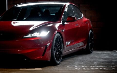 Compressed view of an Ultra Red Tesla Model 3 Performance equipped with 19-inch Gloss Black UP-03 forged wheels by Unplugged Performance, parked against a wall.
