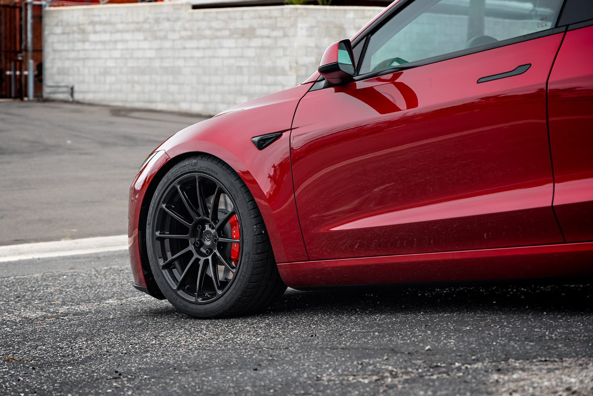 Angled front view of an Ultra Red Tesla Model 3 Performance showcasing 19-inch Gloss Black UP-03 forged wheels by Unplugged Performance, parked on an urban street.