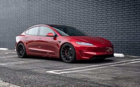 Profile view of an Ultra Red Tesla Model 3 Performance equipped with 19-inch Gloss Black UP-03 forged wheels by Unplugged Performance, parked against a black brick wall.