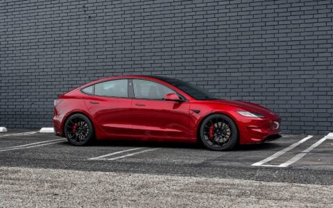 Profile view of an Ultra Red Tesla Model 3 Performance equipped with 19-inch Gloss Black UP-03 forged wheels by Unplugged Performance, parked against a black brick wall.