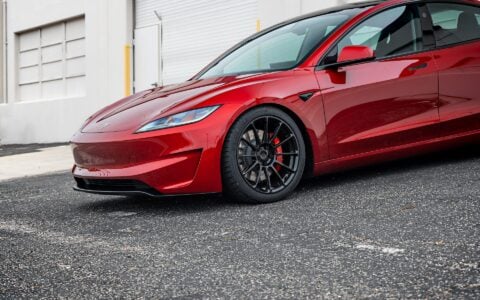 Angled front view of an Ultra Red Tesla Model 3 Performance showcasing 19-inch Gloss Black UP-03 forged wheels by Unplugged Performance, parked on an urban street.