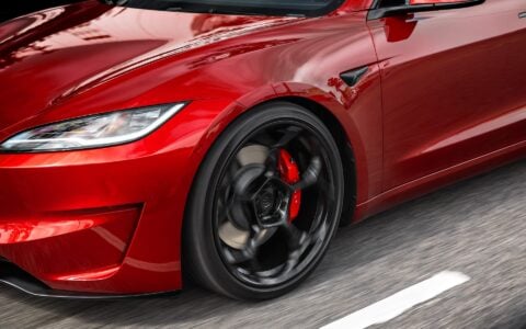 A dynamic front-angle view of an Ultra Red Tesla Model 3 Performance, highlighting its 20-inch Gloss Black UP-05 Forged Wheels from Unplugged Performance.