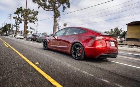 A rolling view of an Ultra Red Tesla Model 3 Performance, emphasizing its 20-inch Gloss Black UP-05 Forged Wheels.