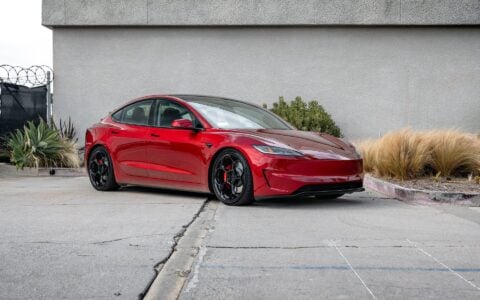 This photo displays the 3/4 view of an Ultra Red Tesla Model 3 Performance, featuring the 20-inch Gloss Black UP-05 Forged Wheels by Unplugged Performance. The image captures the car's modern aesthetics and high-performance wheels.