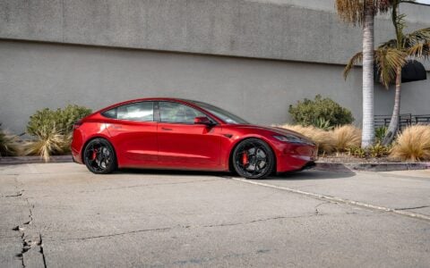 Ultra Red Tesla Model 3 Performance parked, highlighting its 20-inch Gloss Black UP-05 Forged Wheels. The image captures the car's overall design and the wheels' refined look.