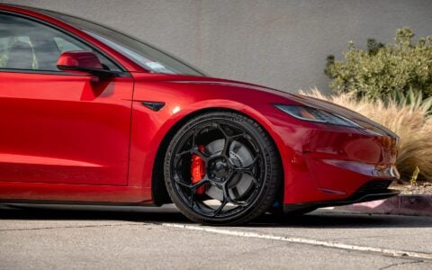 The photo shows an Ultra Red Tesla Model 3 Performance parked, highlighting its 20-inch Gloss Black UP-05 Forged Wheels.