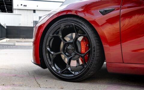 This photo captures a side view of the front wheel of an Ultra Red Tesla Model 3 Performance. The 20-inch Gloss Black UP-05 Forged Wheel, manufactured by Unplugged Performance, is prominently displayed, showcasing its elegant and robust design.